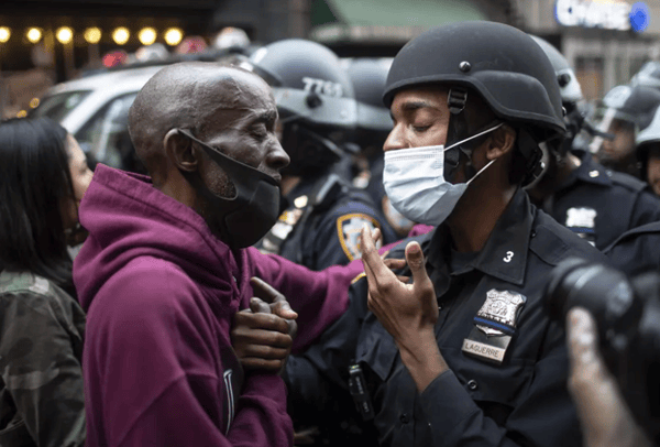 A protester and a police officer hold hands in the middle of a standoff, New York
